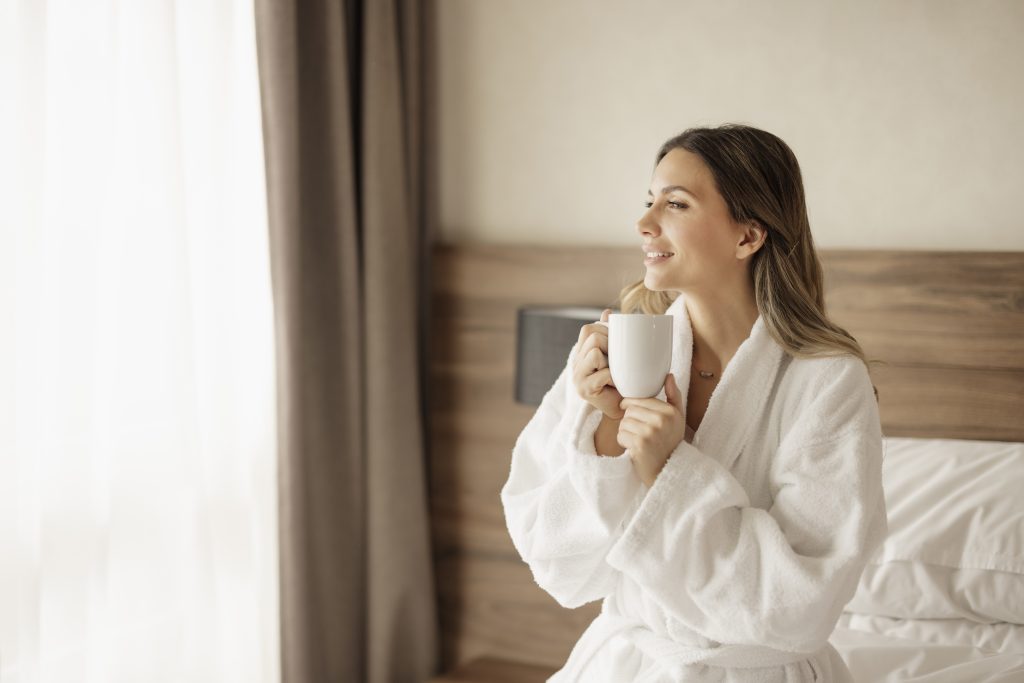 Beautiful woman drinking morning coffee on bed in a hotel powered by Pentair Hotel In-Room Filtration Background