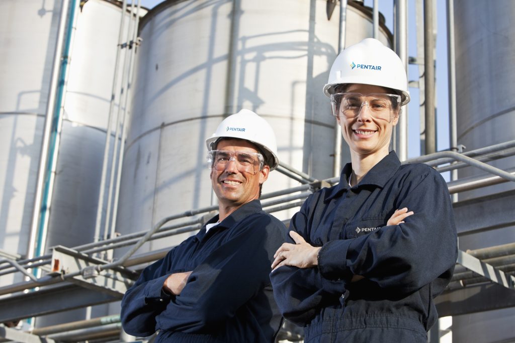 Pentair workers at a chemical manufacturing plant, arms crossed, looking down at the camera and smiling at Pentair Industrial Solutions